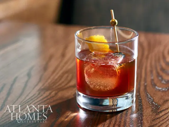 Cocktail with large ice cube and lemon peel on wooden table