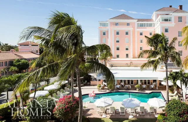 Pink hotel with palm trees and a swimming pool area with lounge chairs and umbrellas.