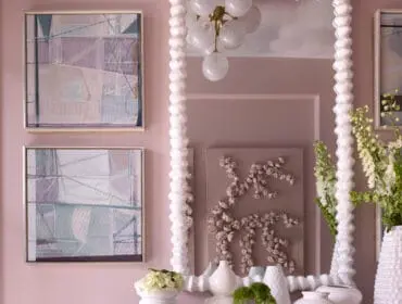 Pink foyer with abstract art, sculptural console table, and white vases.