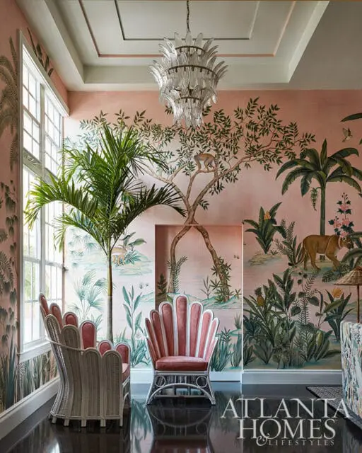 Pink room with tropical mural wallpaper, two shell-back chairs, and a glass chandelier.