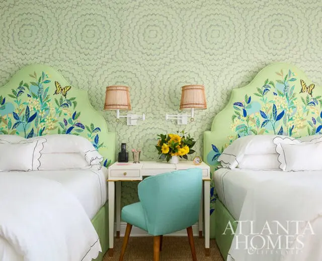 Two beds with floral headboards, a white desk, and mint green chair. Light green floral wallpaper.