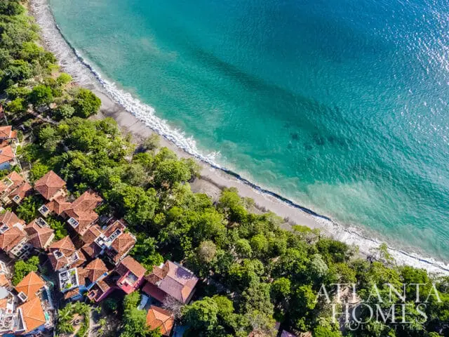 Aerial view of coastal homes nestled among trees next to a turquoise ocean.