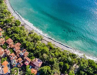 Aerial view of coastal village with red-tiled roofs nestled among lush green trees next to