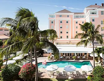 Pink hotel building with balconies overlooking a swimming pool and palm trees.