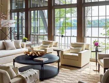 Living room with white sofas, cream armchairs, dark coffee table, and large windows overlooking a