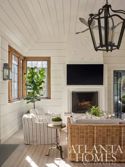 Living room with white shiplap walls, striped armchairs, wicker sofa, and brick fireplace.