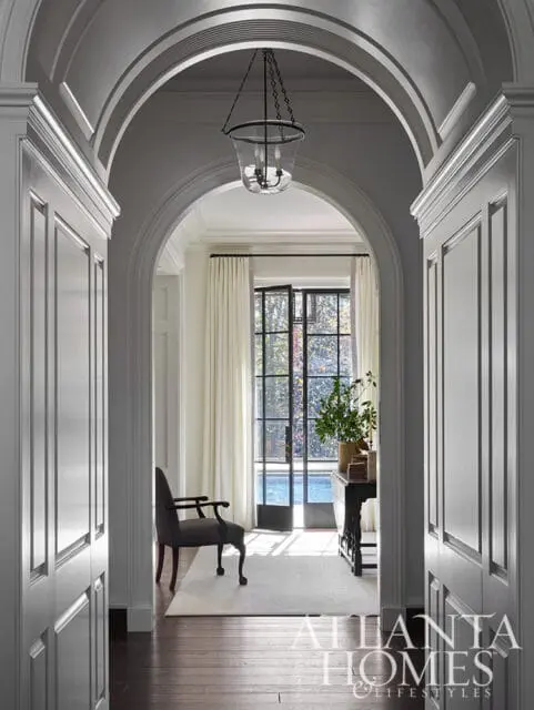 Hallway with arched doorway, paneled walls, dark wood floors, and a glass lantern pendant light.