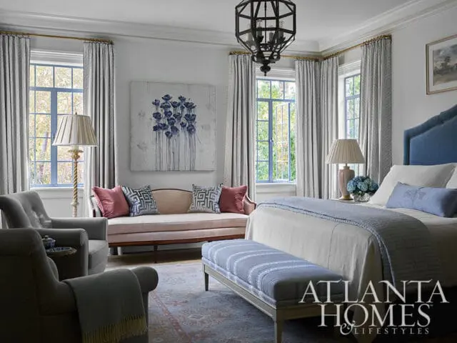 Bedroom with blue upholstered headboard, floral artwork, and gray seating.