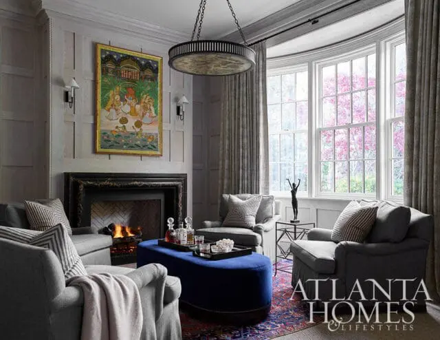 Living room with gray armchairs, blue ottoman, fireplace, and artwork above mantel.