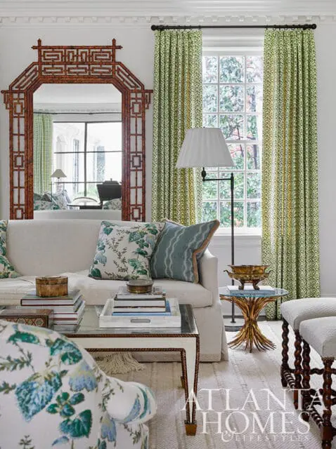 Living room with white sofa, floral pillows, bamboo mirror, and green patterned curtains.