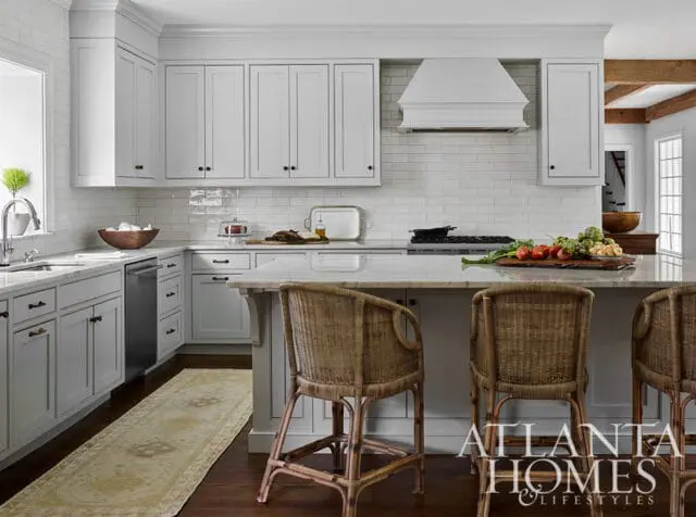 White kitchen with subway tile backsplash, marble island, and wicker bar stools.