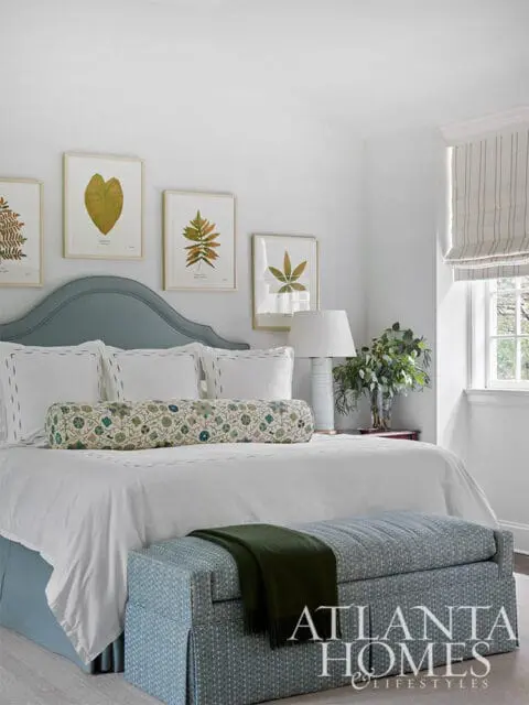 Bedroom with blue upholstered headboard, white bedding, botanical prints, and patterned storage