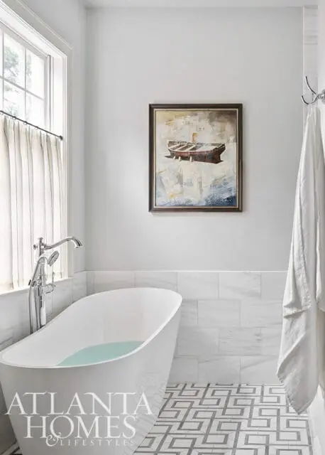 White freestanding bathtub with chrome fixtures, marble tile walls, and geometric floor tiles.