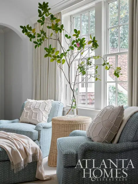 Two blue patterned armchairs with decorative pillows and a wicker side table.