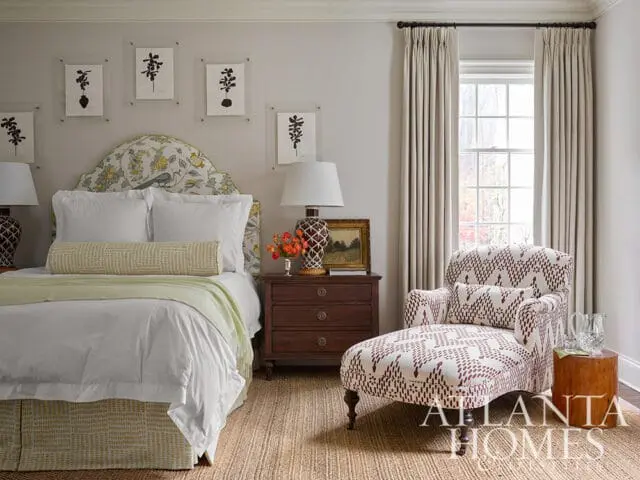 Bedroom with floral headboard, white bedding, patterned chaise lounge, and artwork.