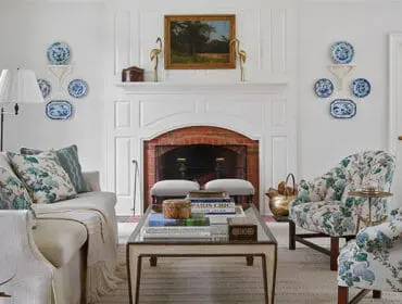 Living room with white sofa, floral armchairs, fireplace, and blue and white plates