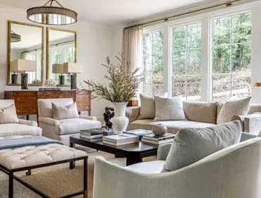 Living room with neutral-toned sofas and chairs, dark wood coffee table, and large windows