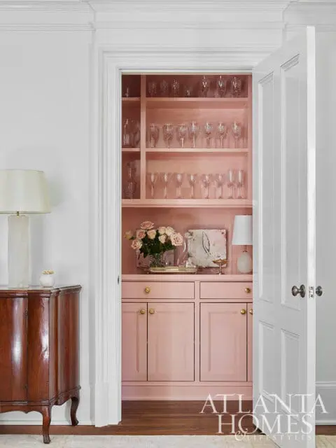 Pink built-in cabinetry with glass shelves displaying glassware.