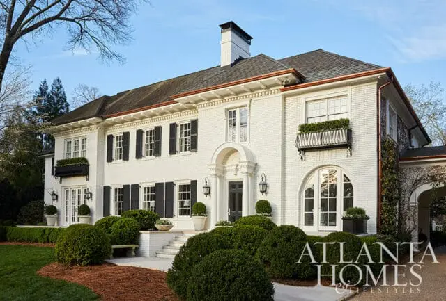 White brick house with black shutters, arched doorway, and manicured hedges.