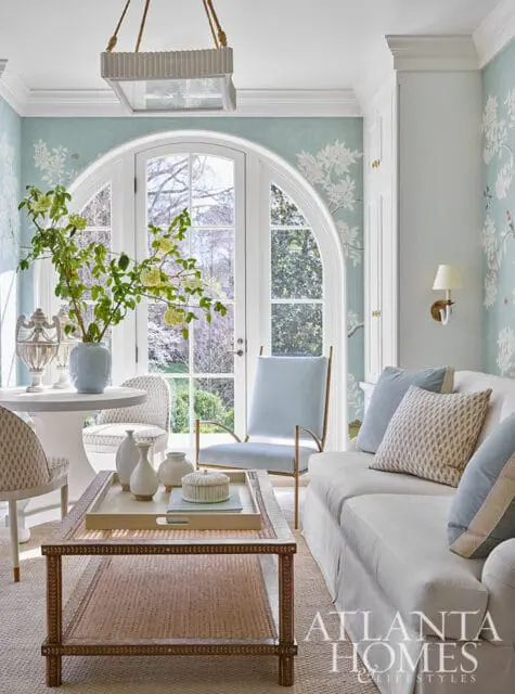 Light blue living room with floral wallpaper, arched window, white sofa, and cane coffee table.