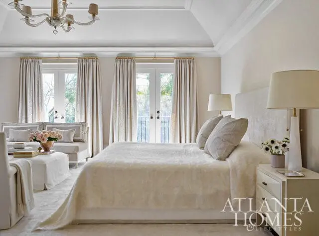 Bedroom with white bedding, upholstered headboard, and double doors with patterned curtains.