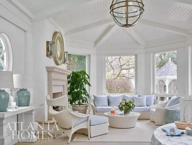 White sunroom with wicker furniture, light blue cushions, and a stone fireplace.