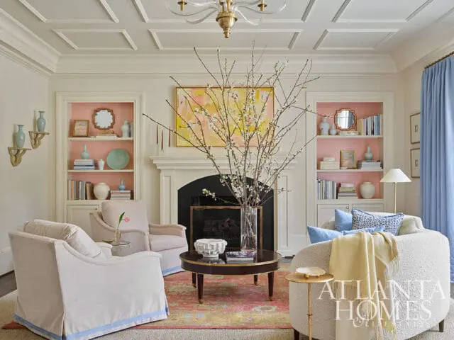 Living room with pink built-in shelves, light blue curtains, and a floral rug.