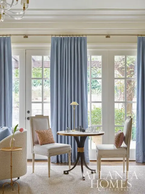 Living room with blue curtains, two chairs, and a round table with a chess set.