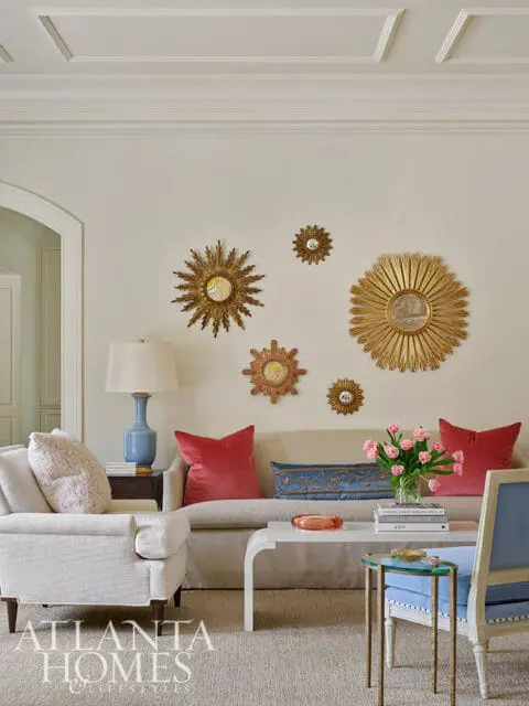 Living room with a beige sofa, red pillows, sunburst mirrors, and a white coffee table.