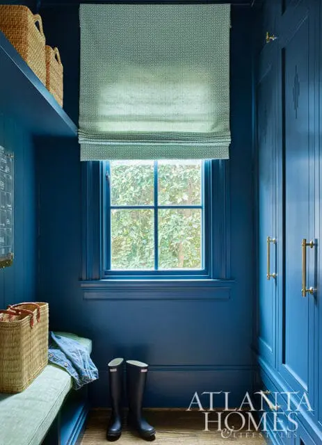 Blue mudroom with a window, bench, baskets, and tall cabinets with brass hardware.