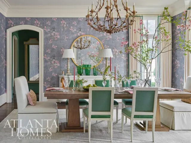 Dining room with floral wallpaper, wooden table, green upholstered chairs, and chandelier.