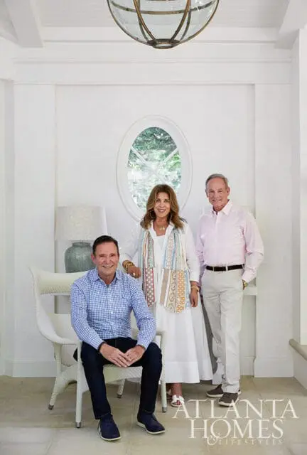 Three people posing in a white room with an oval window and a large pendant light.