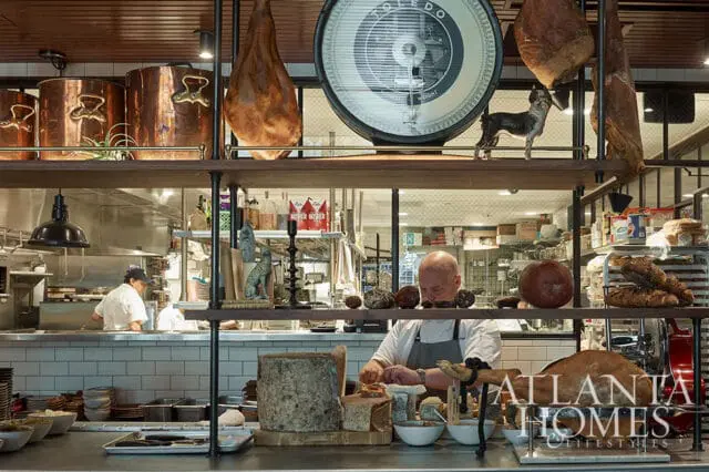 Chef preparing food in a restaurant kitchen with copper pots, hanging meats, and a scale.