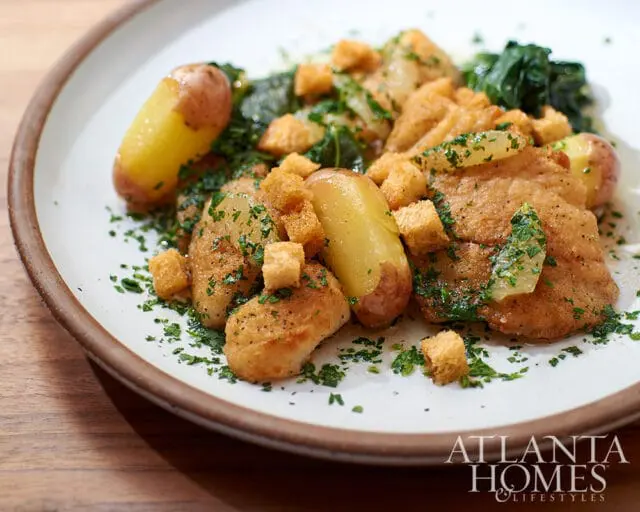 Fried fish with potatoes, croutons, and parsley on a white plate with Atlanta Homes & Lifestyles