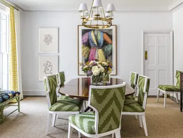 Dining room with oval table, green chevron chairs, colorful art, and floral arrangement.