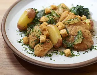 Plate of roasted potatoes, chicken, and greens with croutons and parsley