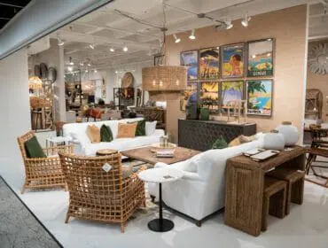 Living room with white sofas, rattan chairs, and vintage travel posters.