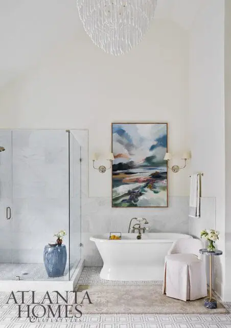 White bathroom with marble shower, freestanding tub, abstract art, and chandelier.