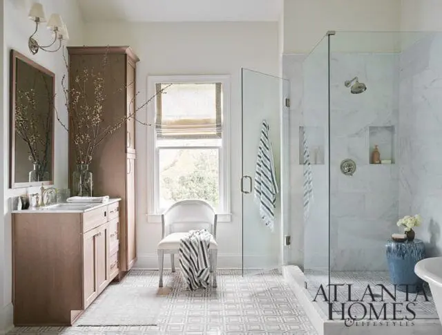 Bathroom with marble shower, wood vanity, and patterned floor. Atlanta Homes & Lifestyles logo