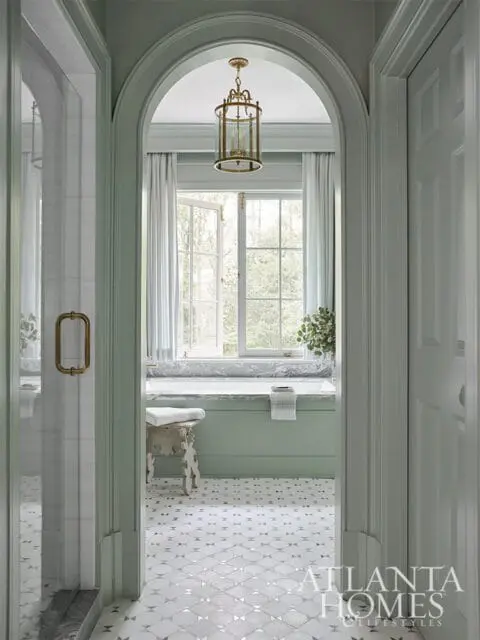 Pale green bathroom with marble bathtub, brass lantern, and patterned tile floor.