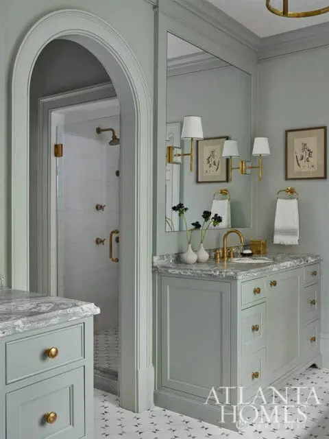 Gray bathroom vanity with marble countertop and brass hardware, arched doorway to shower.