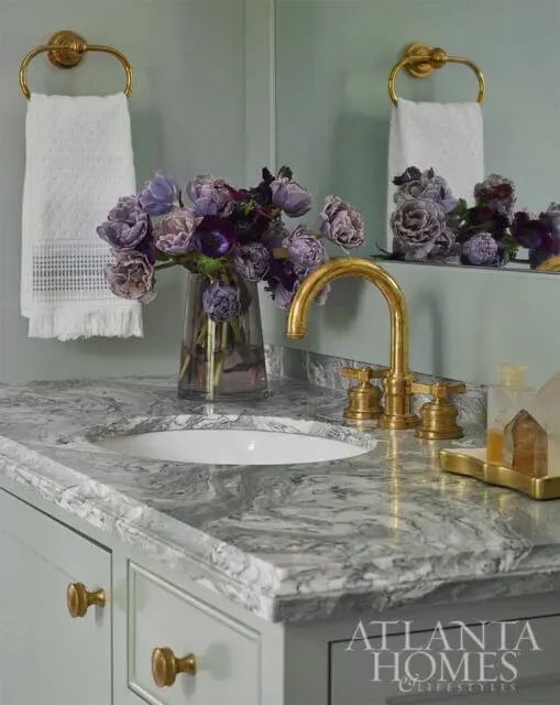 Powder room with marble vanity, gold faucet, and purple floral arrangement.