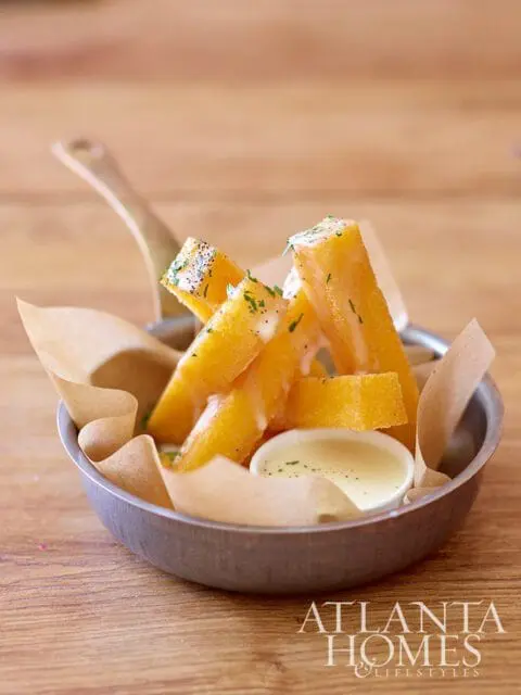 Fried polenta sticks with sauce in a metal bowl with parchment paper
