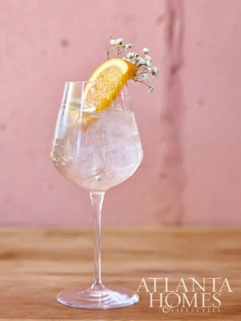 Cocktail with orange slice and flowers in a wine glass filled with ice.