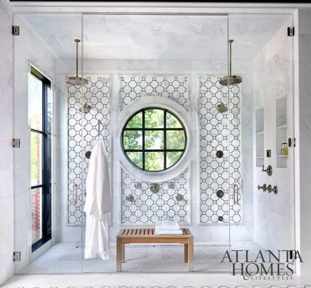 Marble bathroom with geometric tile, circular window, and glass shower
