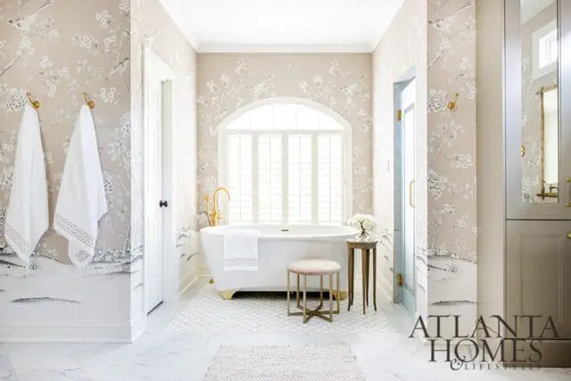 Bathroom with floral wallpaper, freestanding tub, gold fixtures, and marble floors.