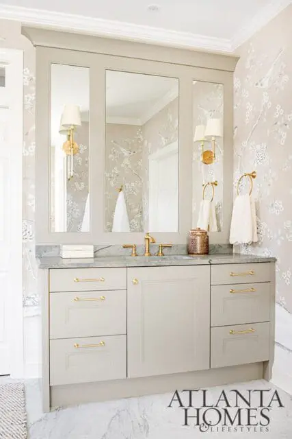 Light gray vanity with brass hardware, marble countertop, and bird-themed wallpaper.