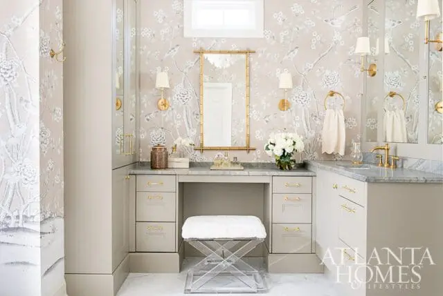 Powder room with floral wallpaper, vanity with marble countertop, gold hardware, and acrylic stool.