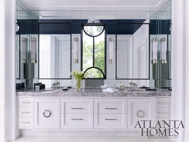 White vanity with marble countertop, double sinks, and mirrored wall with sconces.