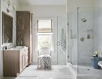 White bathroom with marble shower, wood vanity, and striped towels.